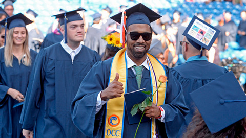 Student in cap and gown with thumbs up at commencement