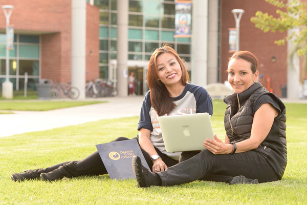2 students sitting on the grass using a laptop