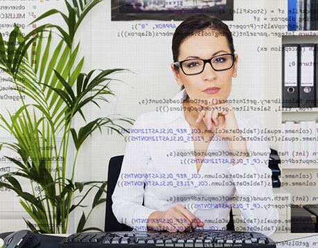 vWoman in white shirt and glasses works at computer and image includes coding as an overlay