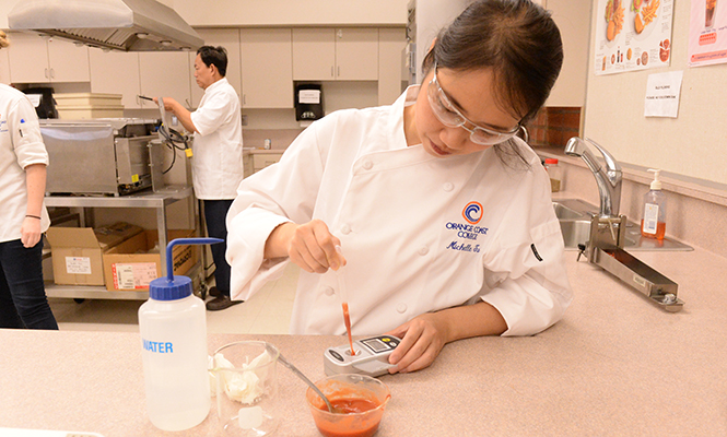 Culinology assistant tests a red sauce with an instrument