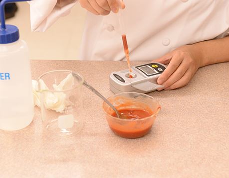 Close up view of a culinology assistant testing a red sauce with an instrument