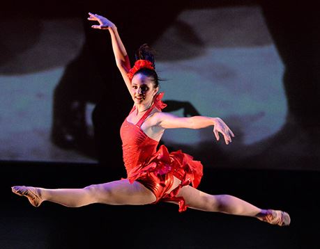 Female dancer in red costume performs a grand jete