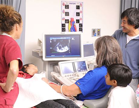 Diagnostic medical sonographer looks at ultrasound with pregnant woman and family