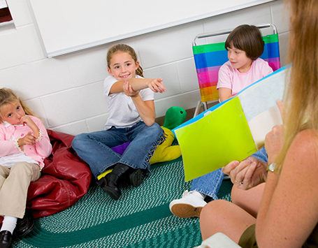 Teacher reads a book to three toddlers sitting on the ground in front of her