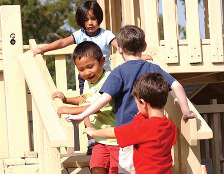 Four preschool students run up stairs together on a playground