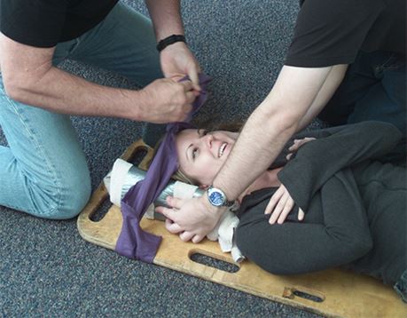 Two male EMTs secure female patient on spineboard