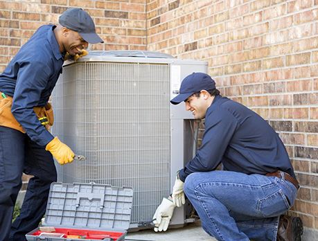 Two HVACR workers inspect an air-conditioning unit outside of a building
