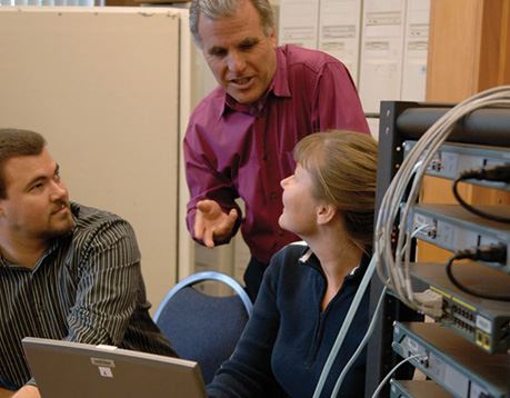 Three network technicians talk next to computer