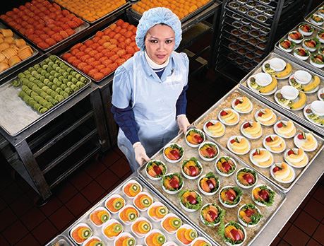 Nutritionist smiles in front of a table full of prepared fruit dishes