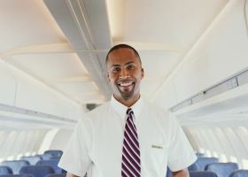 A male flight attendant standing in an airplane aisle smile at the camera