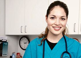 Medical assistant with stethoscope and vitals chart smiles at camera