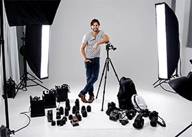 Male photographer poses for camera in middle of studio with his equipment