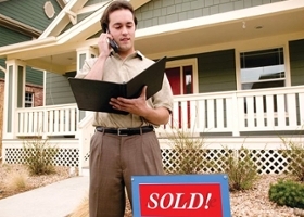 Male real estate broker talks on the phone in front of a sold house