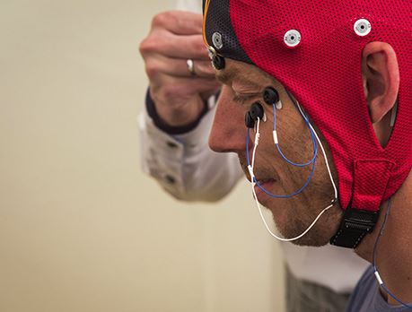 Polysomnographic technologist places electrodes on a man wearing a EEG cap