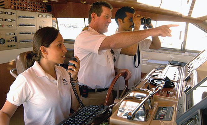 Three professional mariners navigate a ship while one looks through binoculars