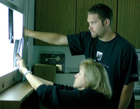 A student standing next to an instructor views an x-ray displayed on a film illuminator
