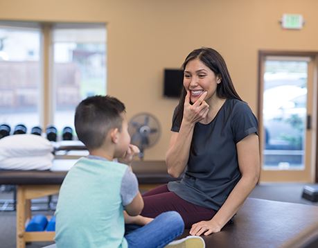 Speech-language pathology assistant demonstrates to a child holding two fingers around her mouth