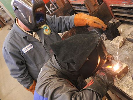Two welders in welding gear work in welding lab