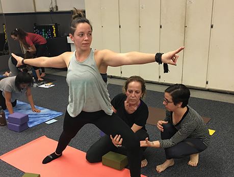 Female yoga instructor corrects student's warrior two pose