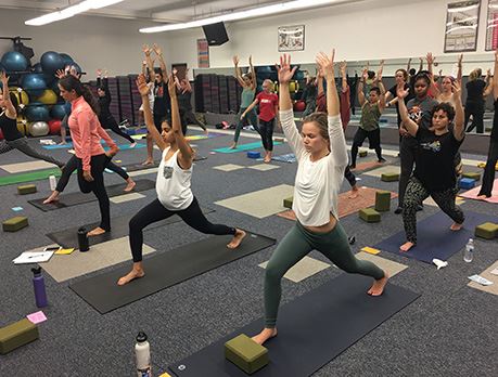 A class of yoga students stand in warrior one pose