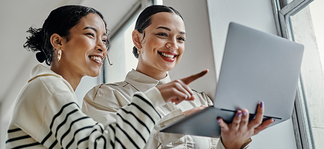 Two women smiling and collaborating while working on a laptop.