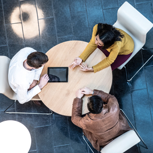 Three students engaged in a discussion around a round table.