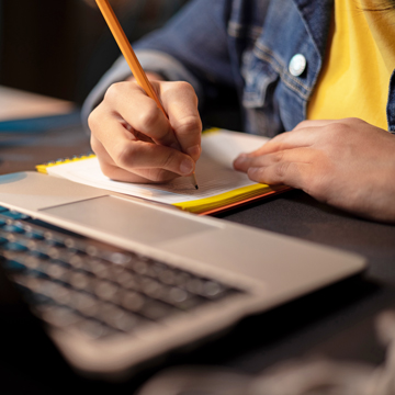 Person writing on a pad next to a laptop
