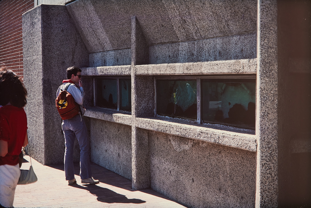 Student with red backpack observing aquariums outside, 1984.