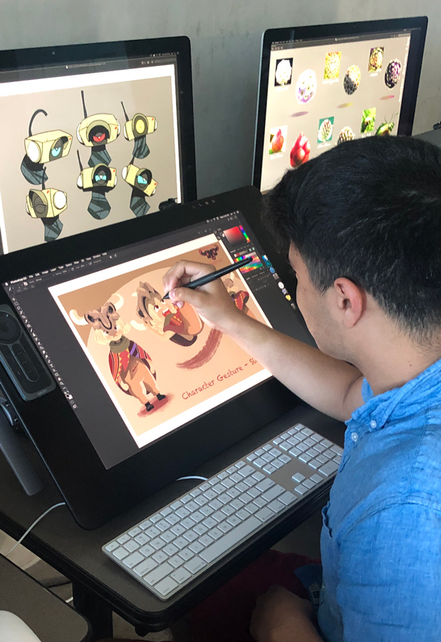 An artist creating character designs on a digital drawing tablet, with various illustrations displayed on screens in the background.