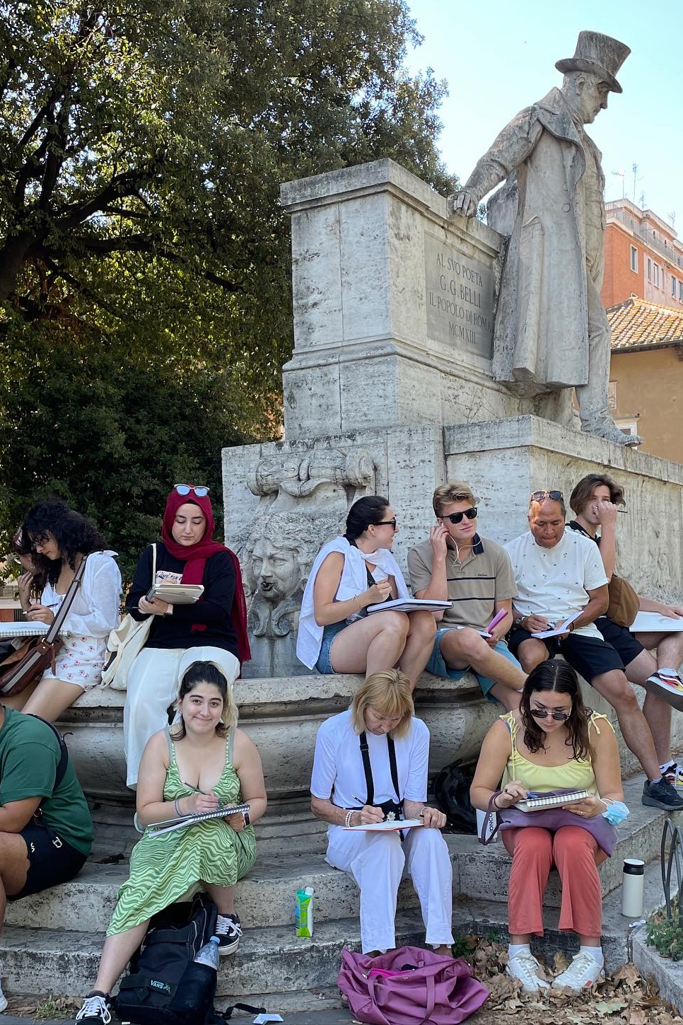 A group of diverse individuals sketching near a historical statue in an outdoor setting. The scene captures a creative atmosphere among artists absorbed in their drawings.