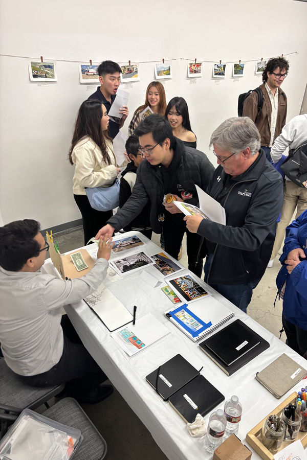A group of people interacting at a display table, with attendees engaged in conversation and examining project materials.