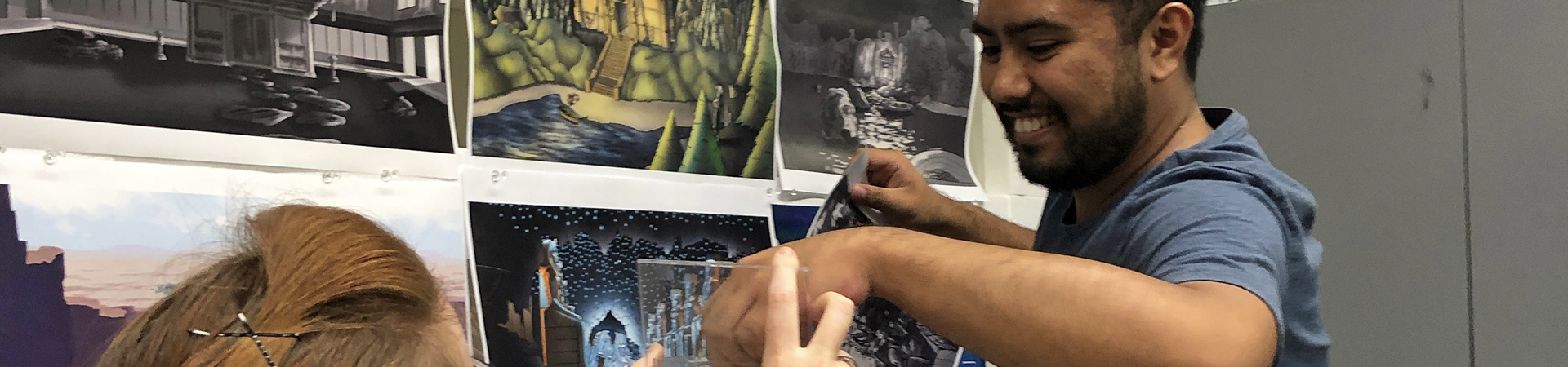 2 students hanging printed artworks on a wall