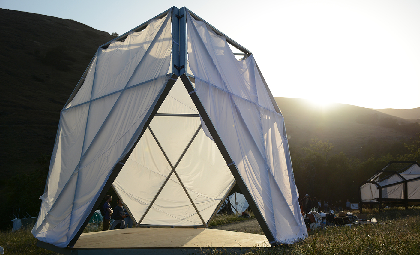 Tetrahedron structure with soft fabric walls. In background is sunny, grassy, and hilly landscape.