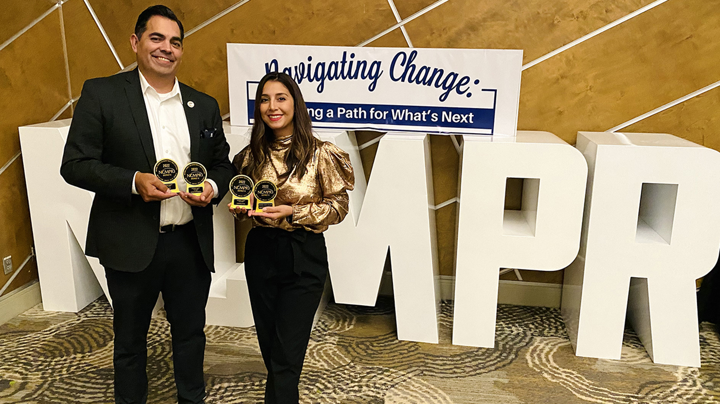 photograph of juan gutierrez and andrea rangno from marketing and pr team holding awards in front of large letters spelling out NCMPR