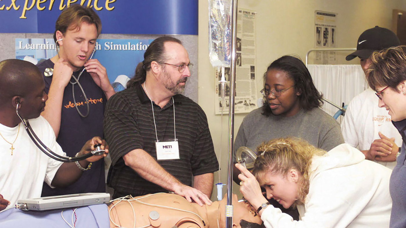 photo of students and instructor surrounding a medical manikin. instructor is explaining something to students related to respiratory care. 