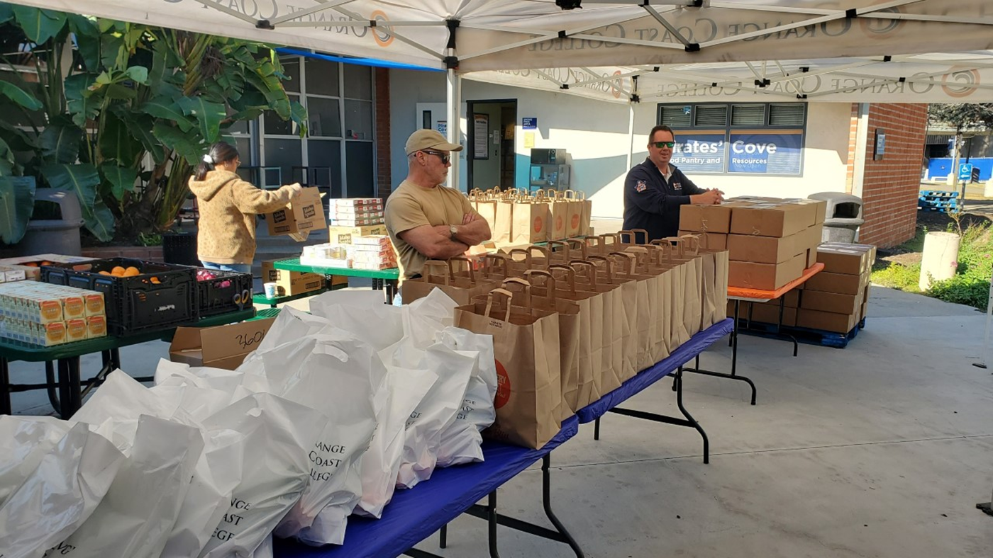 photograph of food distribution volunteers standing next to table with brown paper bags filled with food