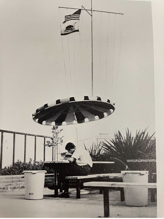 Flag pole with a student sitting at a bench seen from 1950's