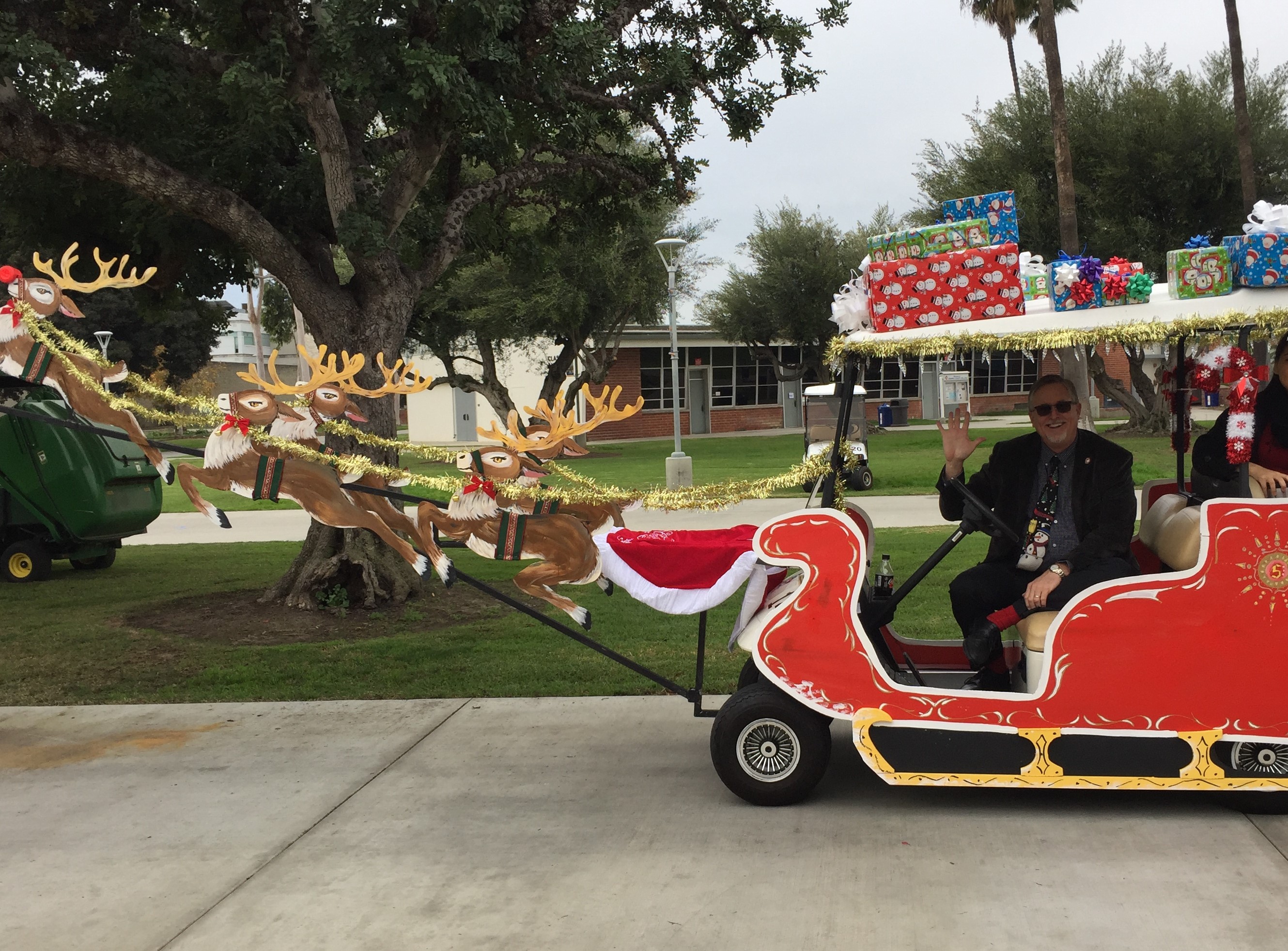 a person in a red and white sleigh (golf cart) with reindeers and presents on it