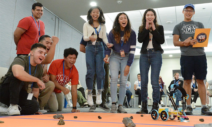 A group of students standing together watching a robot move.