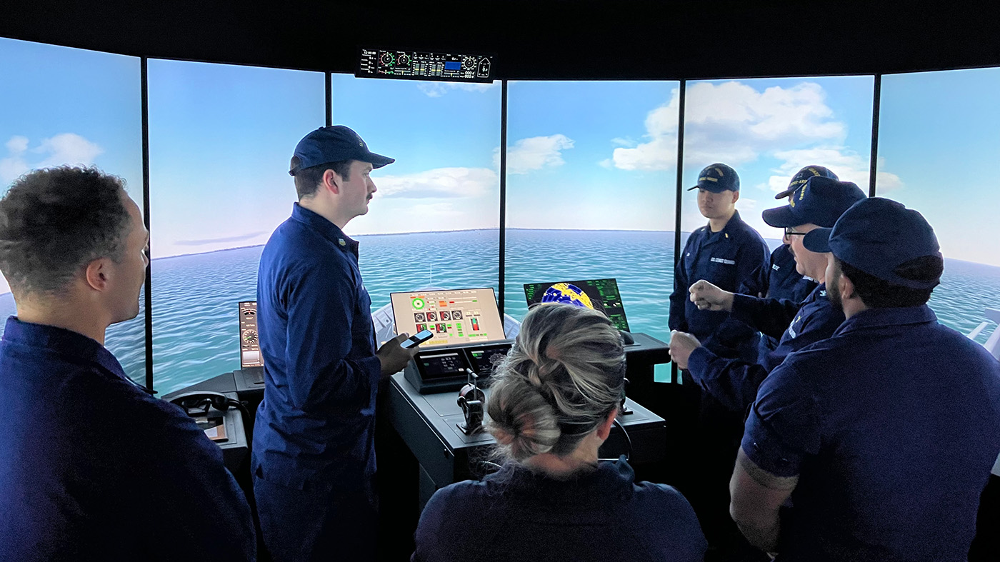 Seven people standing around a navigation bridge simulator