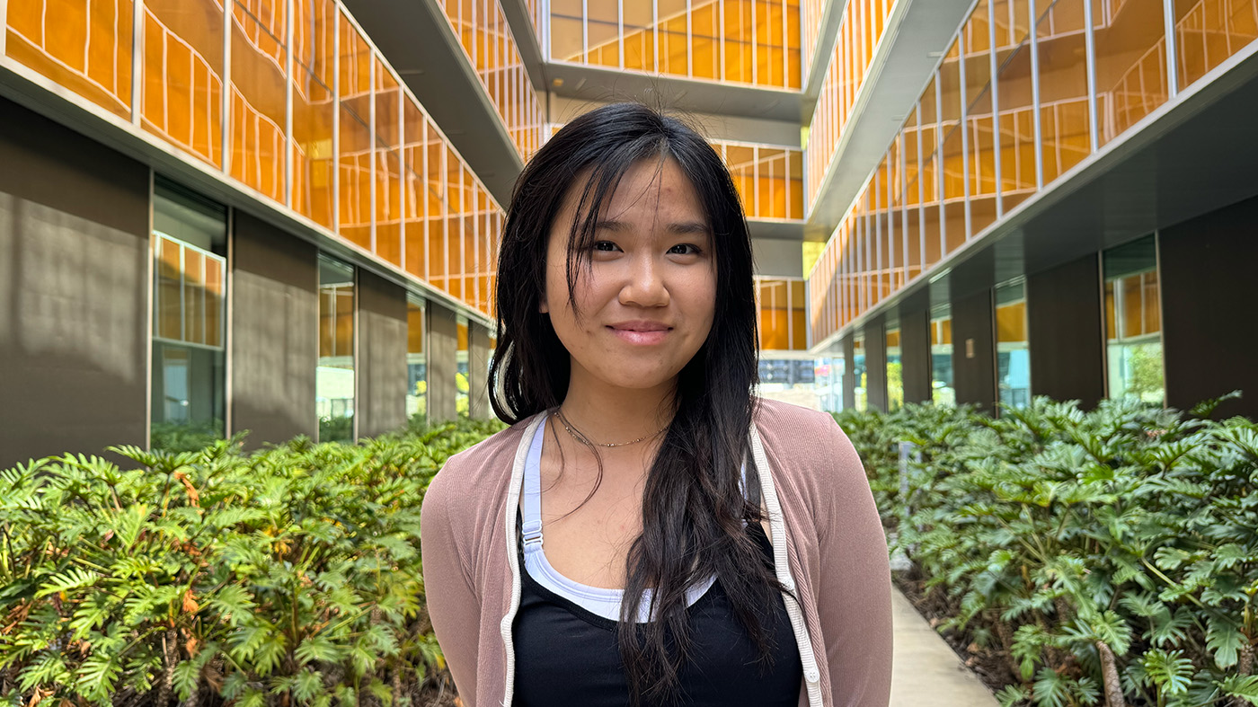 One smiling female standing in the middle of a walkway, orange tinted panes behind her