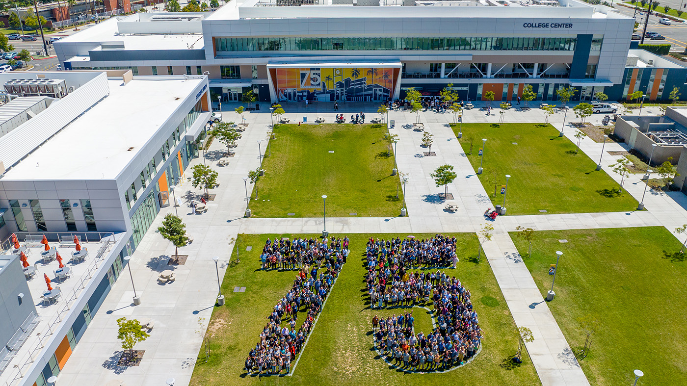 Aerial view of a group of people forming the number 75 on a grassy area in front of a modern building 