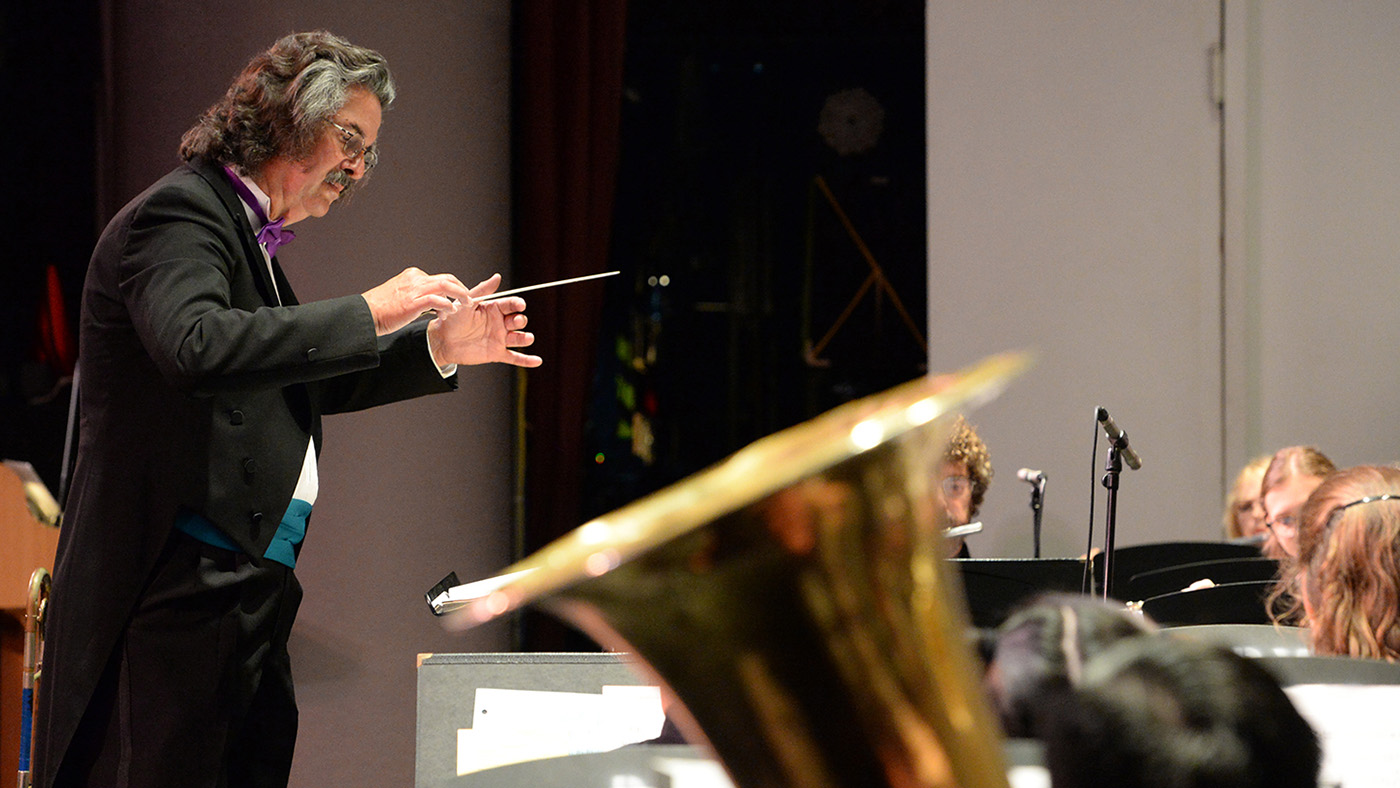 A conductor in formal attire with a bow tie is leading an orchestra on stage