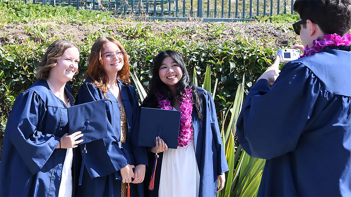 3 students in graduation gowns posing for a photo