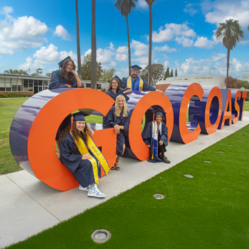 A group of students in cap and gown standing by the GoCoast monument letters.