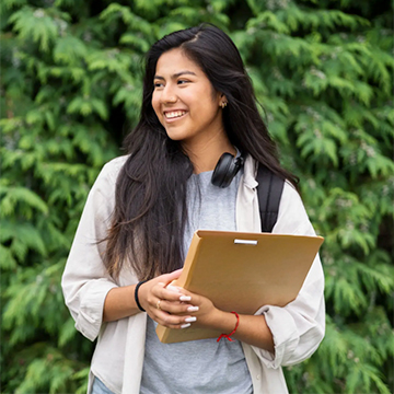 A student wearing headphones around the neck and holding a binder.