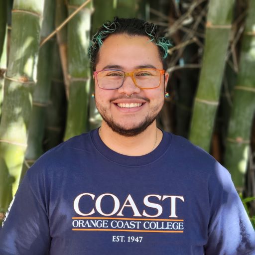 LGBTQIA+ project specialist Caleb standing in front of bamboo and smiling.