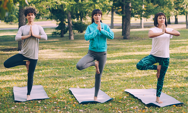 Three women practicing yoga outdoors on yoga mats.